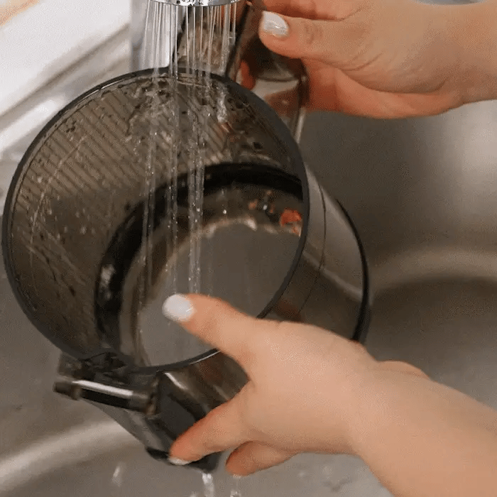 Person washing the kuvings auto8 case under running water in a sink.