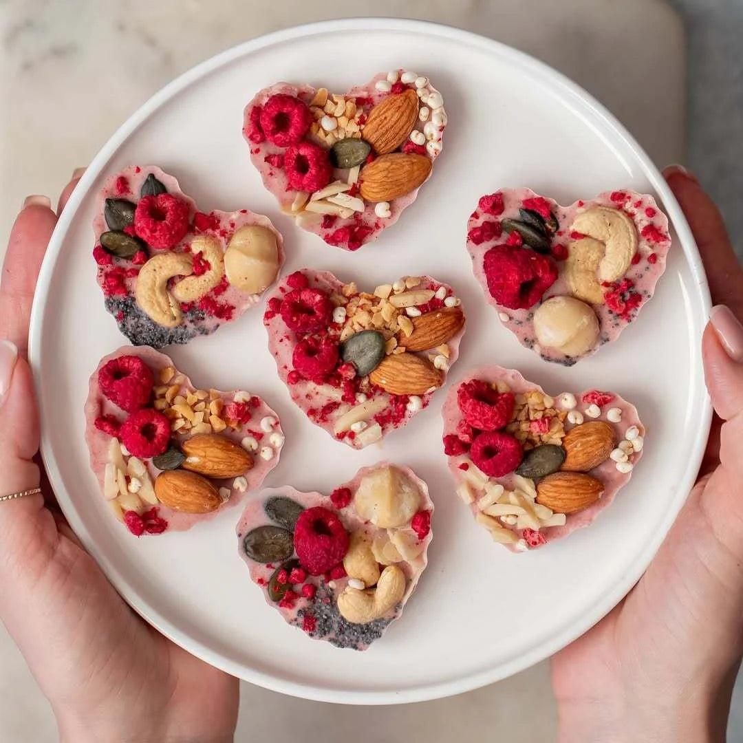 Heart-shaped snacks with berries and nuts on a white plate held by hands.