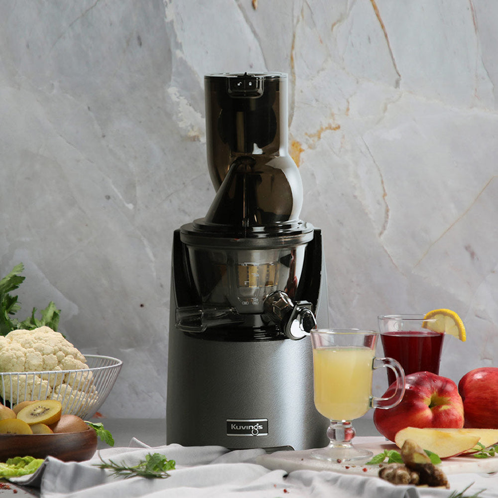 Kuvings EVO820 gunmetal grey slow juicer with fresh fruit and vegetable juices in a modern kitchen setting.