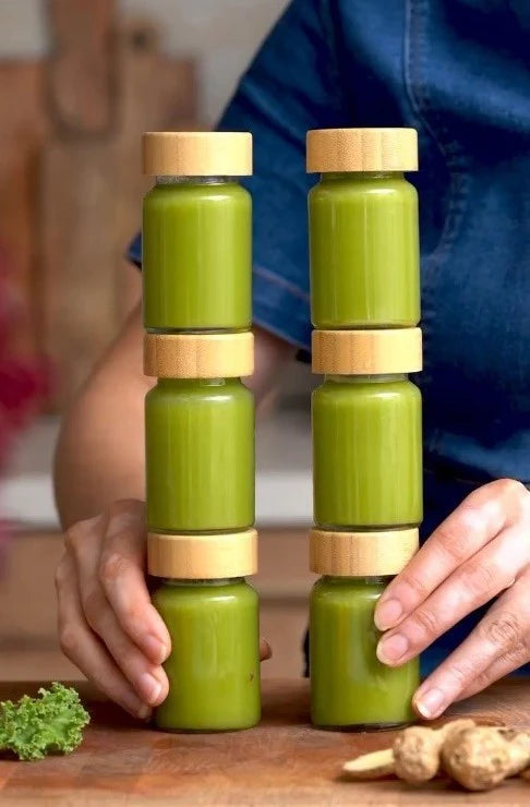Kuvings green ceramic juice bottles with wooden lids held by a person on a wooden surface for homemade juice storage.
surface.