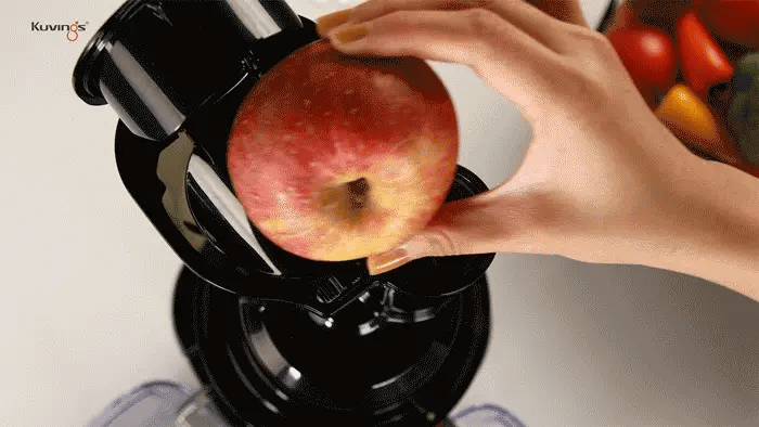 Hand placing an apple into a Kuvings REVO830 with vegetables in the background