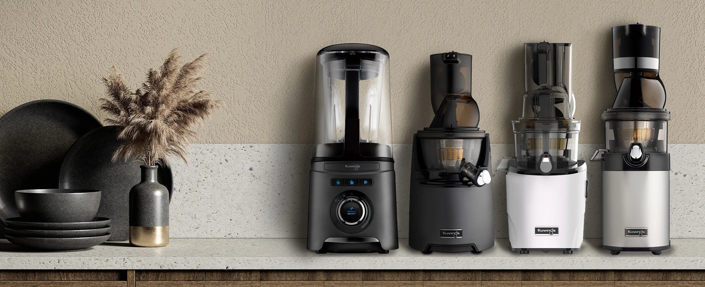 Straight-on, eye-level wide shot of a premium lineup of Kuvings kitchen appliances arranged on a stone counter, displaying from left to right: a vacuum blender, the EVO830 slow juicer, the REVO830 slow juicer, and the CS600 Chef commercial slow juicer.