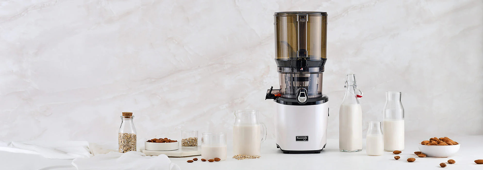 Kuvings AUTO10 slow juicer with homemade almond milk, almonds and oat ingredients on a bright kitchen counter.