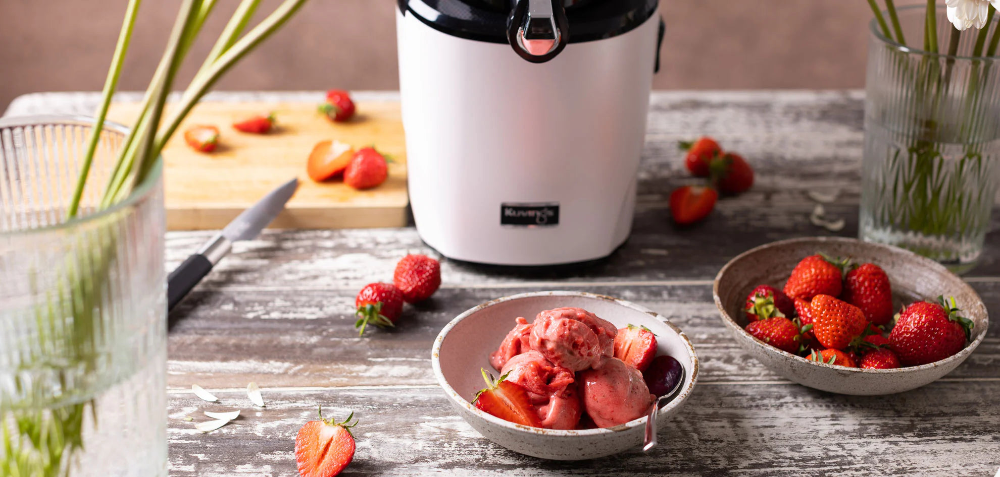 Kuvings AUTO10S white slow juicer with homemade strawberry sorbet and fresh strawberries on a kitchen table.