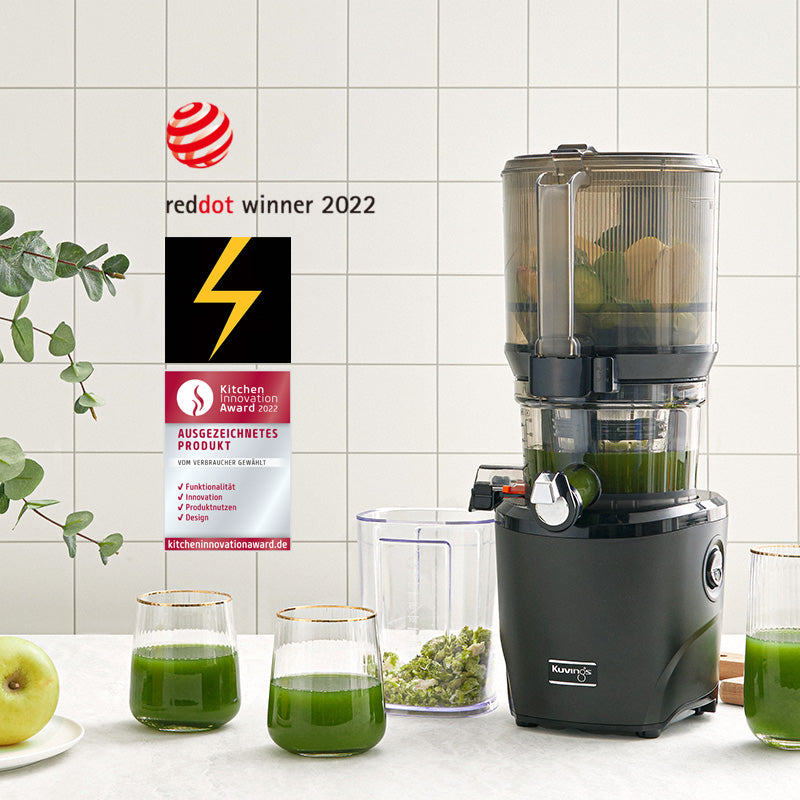 Studio product shot of a black Kuvings AUTO10S slow juicer with glasses of green juice, featuring emblems for the Red Dot Winner 2022 and German Kitchen Innovation Award.