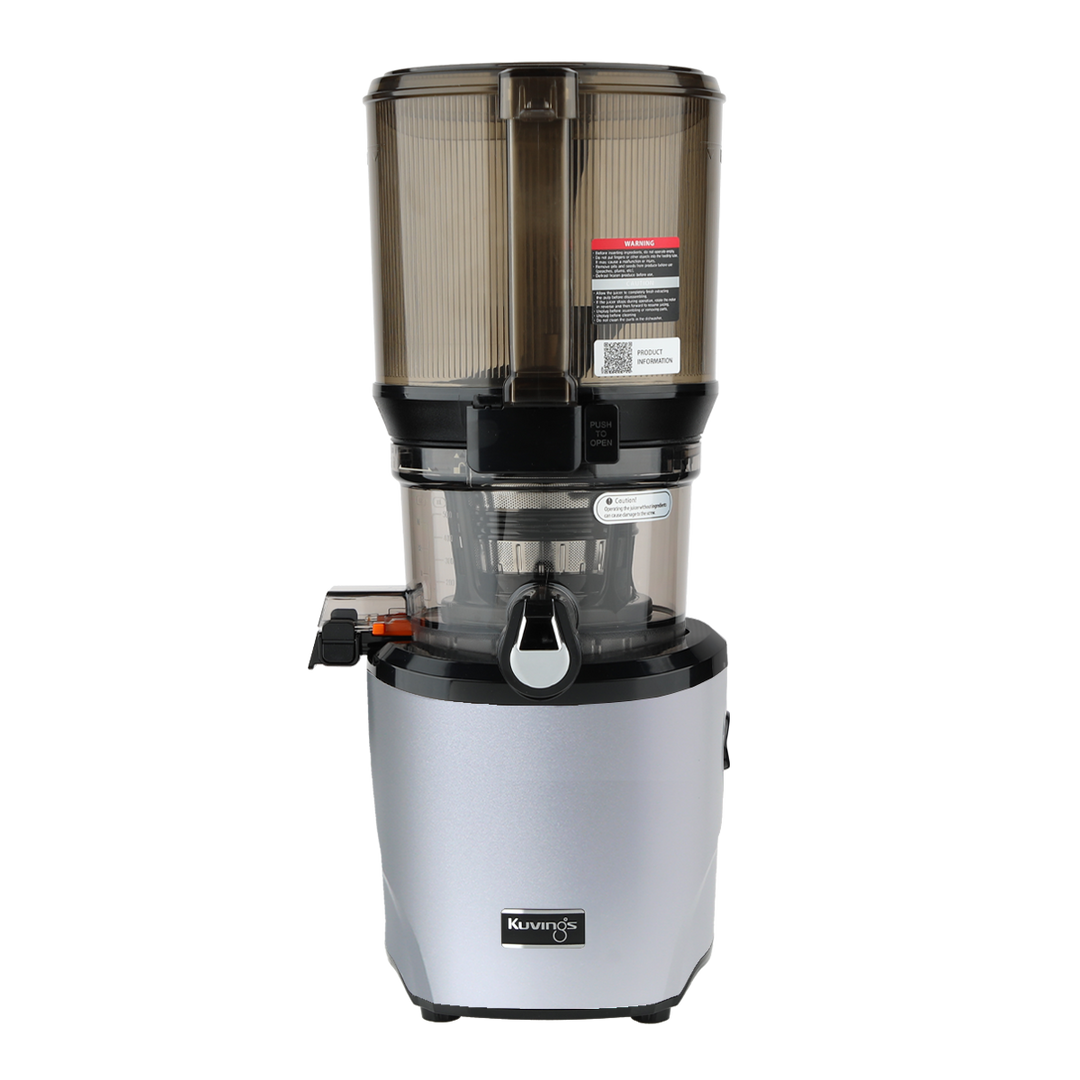 Straight-on studio product shot of a silver Kuvings AUTO10S whole slow juicer with its large transparent grey mega-hopper container attached, showing the integrated handle on the hopper front, isolated against a transparent grid background.