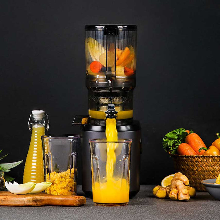 Kuvings AUTO6 black slow juicer making fresh orange juice with carrots, ginger and citrus fruits.