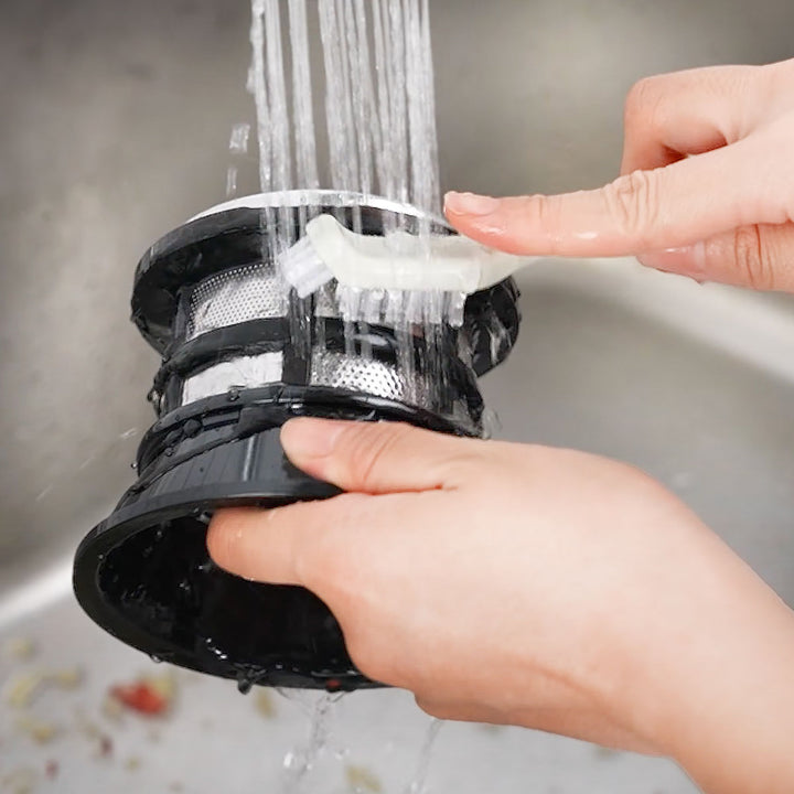 Kuvings AUTO6 slow juicer juice strainer being cleaned with a brush under running water for easy maintenance.