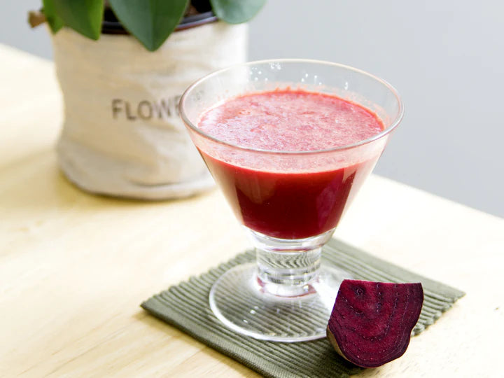Glass of red smoothie on a coaster with a beetroot and plant in the background