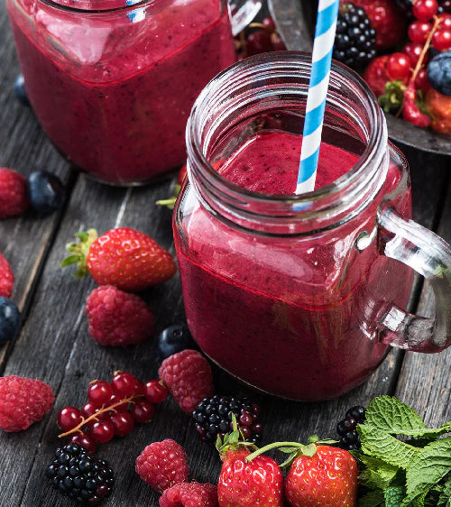 Glass jar with a handle filled with a red smoothie, surrounded by fresh berries on a wooden surface.