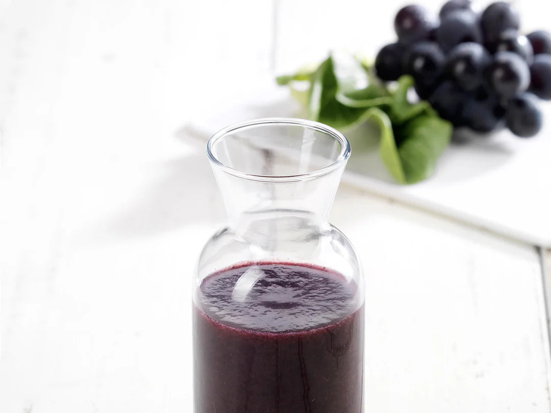 Glass bottle of purple grape juice with grapes in the background