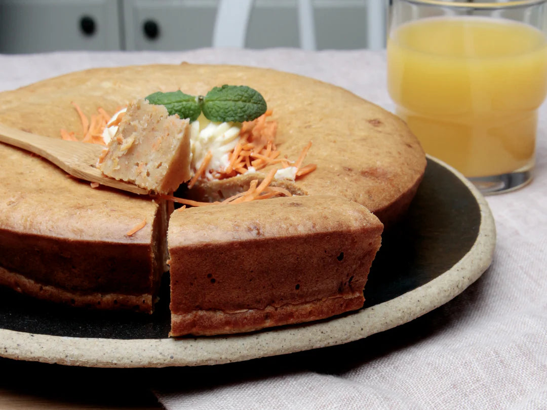 Carrot cake with a slice removed on a plate next to a glass of orange juice.