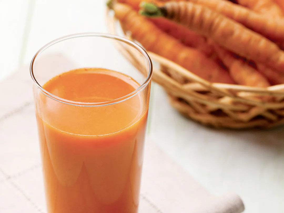 Glass of carrot juice with a basket of carrots on a white surface