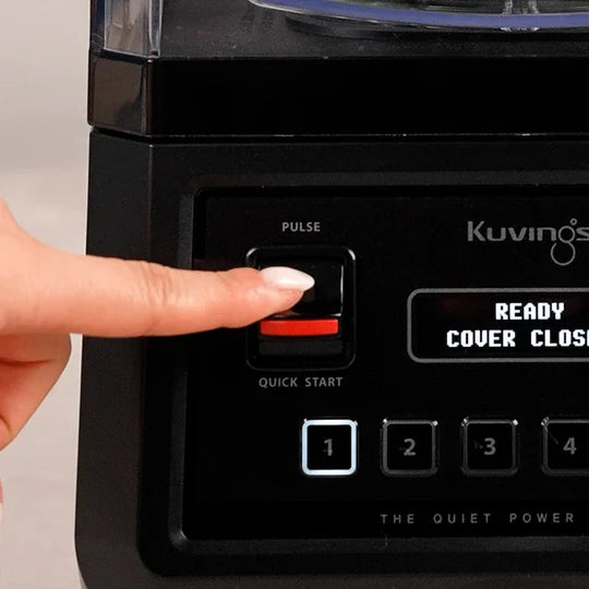 Extreme close-up front view of a finger pressing the red-accented pulse quick-start switch on the Kuvings CB850 blender control panel, with the display showing 'READY COVER CLOSED'.