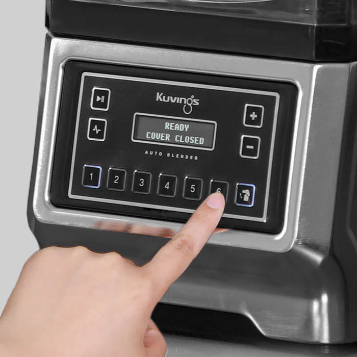 Angled close-up view of a finger pressing button six on the silver metallic control panel of a Kuvings CB980 Auto Blender, with the digital screen displaying 'READY COVER CLOSED'.