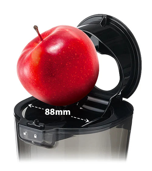 High-angle close-up studio shot showing a large red apple sitting inside the wide-mouth flip-gate feeding chute of a Kuvings Chef CS700 commercial slow juicer, accented by a white double-sided measurement arrow indicating an 88mm diameter against a white background.