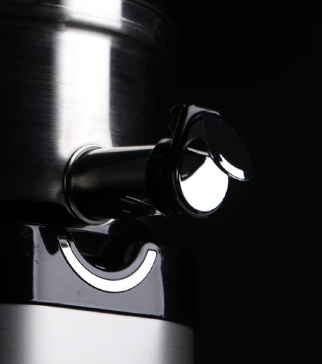 Three-quarter close-up studio product shot of the stainless steel juice spout and chrome-accented smart cap of a Kuvings Chef CS700 commercial slow juicer, dramatically lit against a solid black background.