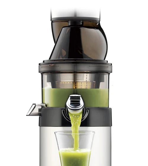 Straight-on, medium studio shot of the top section of a Kuvings CS600 Chef commercial slow juicer showing the wide-mouth feeding chute assembly and clear juicing bowl as fresh green juice pours from the open chrome smart cap spout into a glass against a white background.