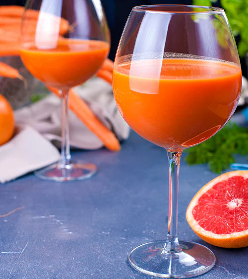 Two glasses of carrot juice with carrots and a grapefruit on a blue surface