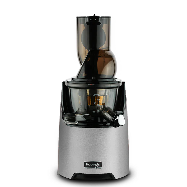 Three-quarter studio product shot of a Kuvings EVO820 whole slow juicer featuring a textured silver metallic motor base with a black Kuvings logo badge, assembled with its dark translucent juicing drum and wide-mouth O-shape feeding chute against a transparent checkered background.