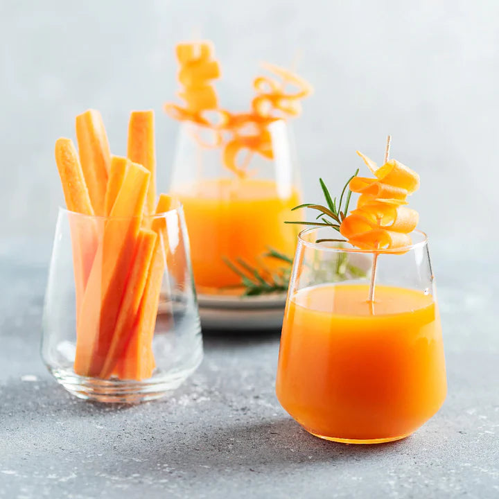 Two glasses of orange juice with carrot sticks on a light gray background