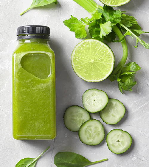 Green smoothie in a bottle with lime, cucumber, and celery on a light surface