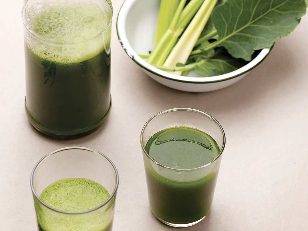 Green juice in glasses with a bowl of green vegetables on a light surface