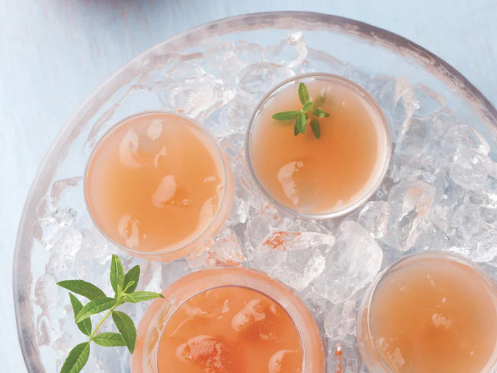 Three small cups of pink drink with a sprig of mint on a bed of ice.