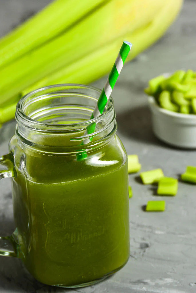 Green smoothie in a mason jar with celery sticks and green vegetables in the background.