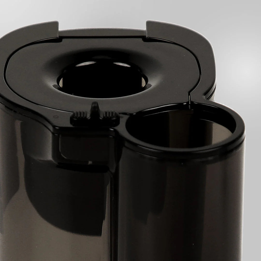 Close-up studio shot of the closed black dual-entry feeding chute assembly on a Kuvings REVO830 whole slow juicer, showing the circular flip-gate and the smaller round ingredient slot against a grey background.