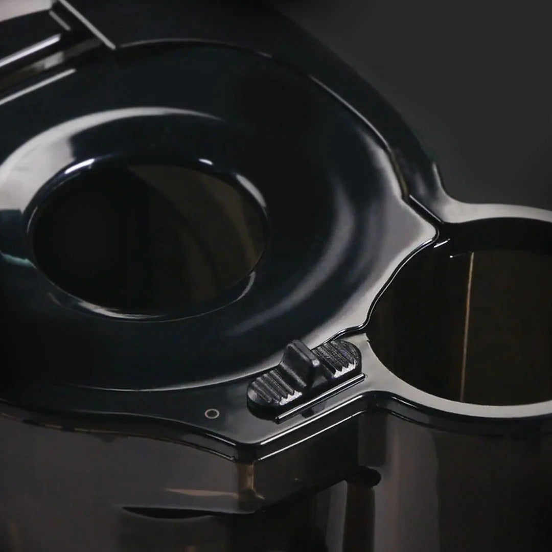 Close-up studio shot of the black glossy feeding chute on a Kuvings REVO830 whole slow juicer, focusing on the textured plastic safety slide lock slider button on the dual-entry lid assembly.