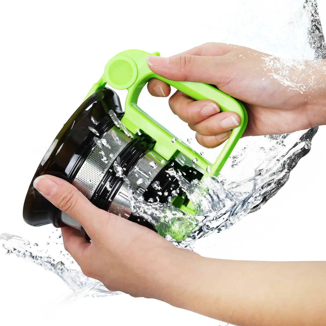 Studio product shot of hands washing a Kuvings slow juicer mesh strainer with the green rotary cleaning brush tool under splashing water, isolated against a transparent grid background.