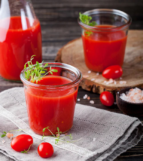 Tomato juice in glass jars with cherry tomatoes on a wooden surface