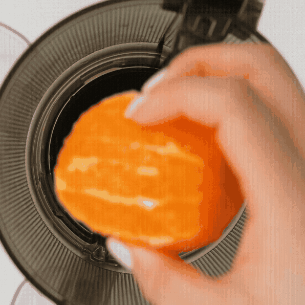 Kuvings AUTO10 juicer GIF showing orange pieces being added into the feeding chamber for fresh homemade juice.